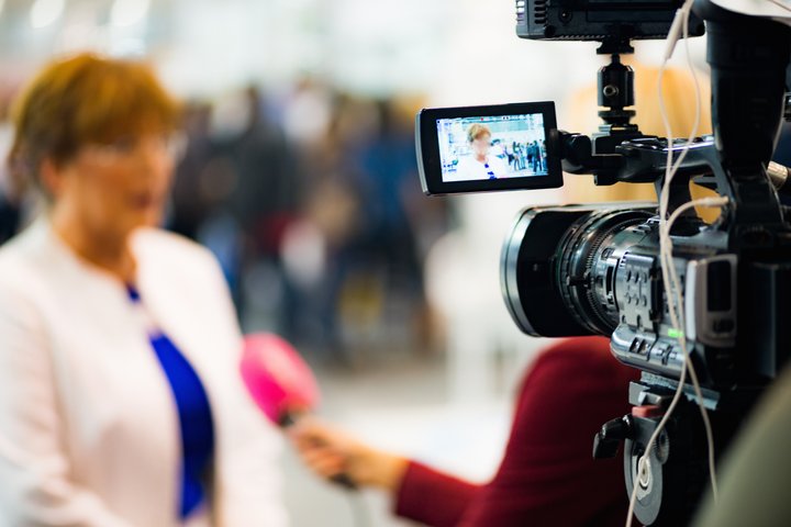 A woman is being interviewed on camera. The camera is in focus, the woman is blurred.