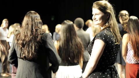 A crowd of women face forward. One woman faces the camera.
