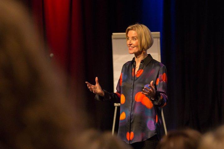 A woman stands in front of a clipboard, smiling and gesturing at an audience