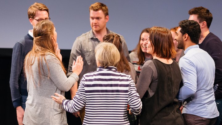 RADA Business course participants huddle together in a theatre, discussing something.