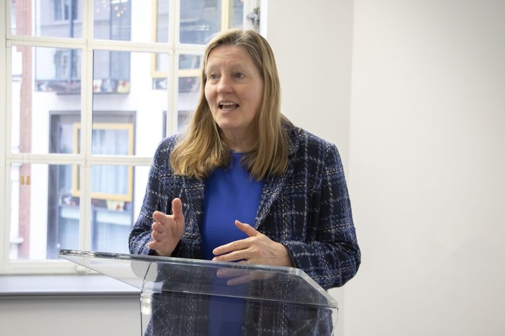 Woman standing at a small podium, delivering a presentation