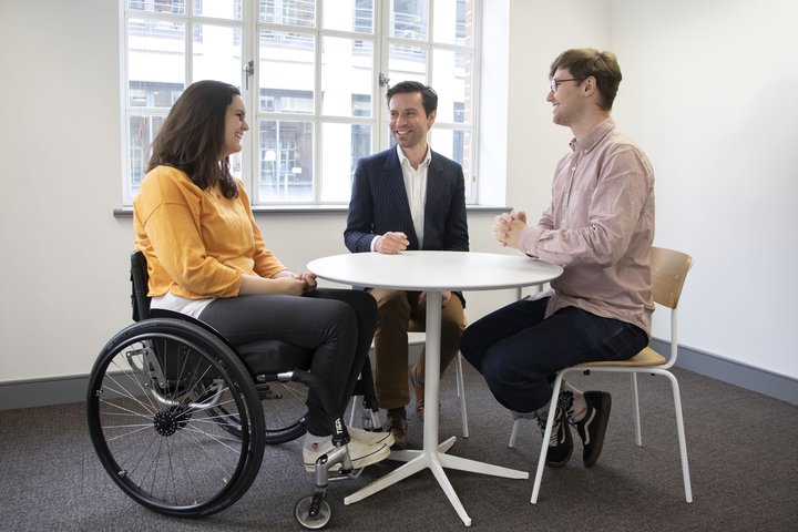 3 people sit around a table, talking